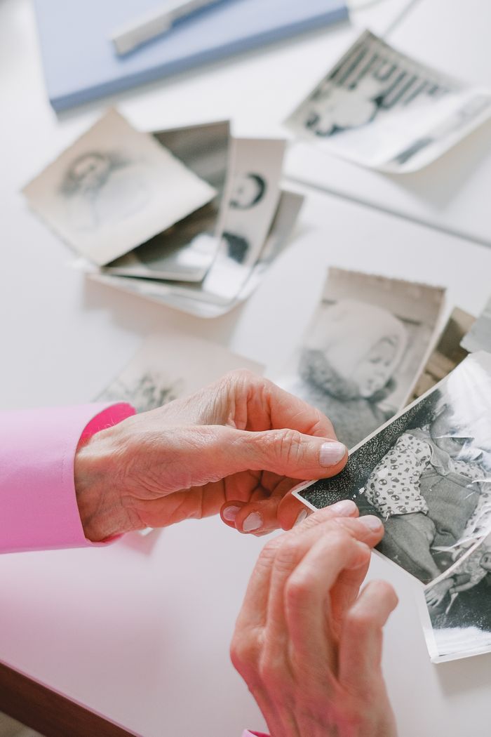 Mastering the First Impression: Your intriguing post title goes here An elderly person with pink sleeves is reviewing nostalgic black and white photographs at a table.