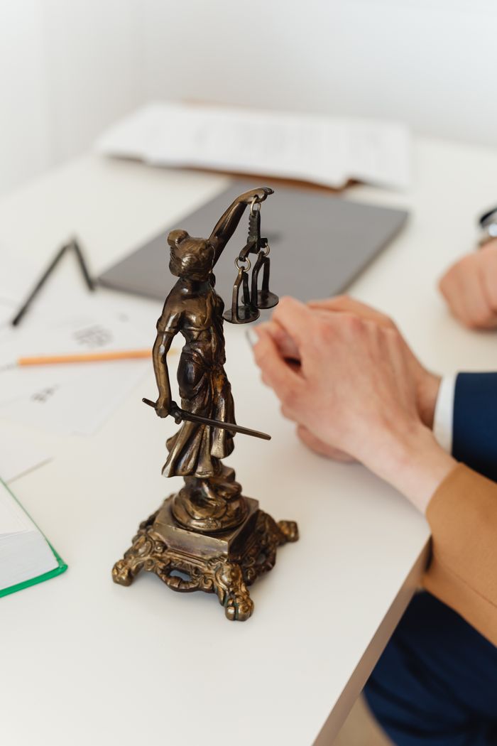 The Art of Drawing Readers In: Your attractive post title goes here Bronze Lady Justice statue on a white office desk with hands in the background. Symbol of law and fairness.